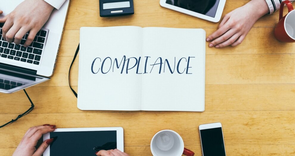 Compliance headline on paper notebook at small business office desk with young adult workers